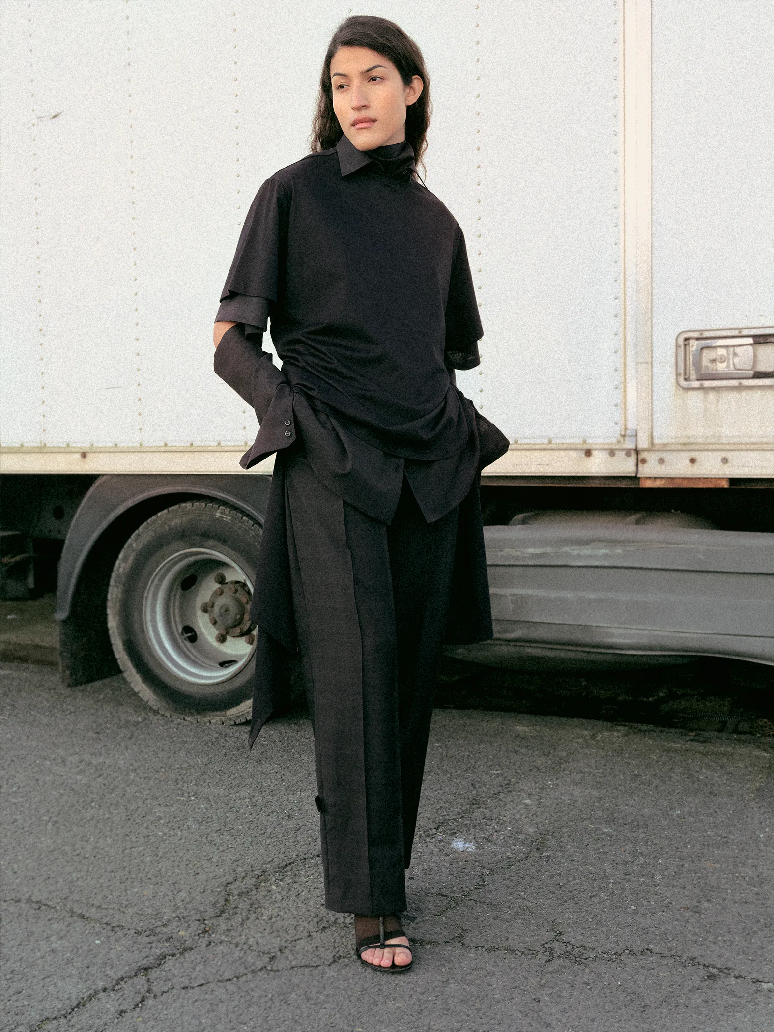 Model wearing a layered black Drop 3 look beside a truck